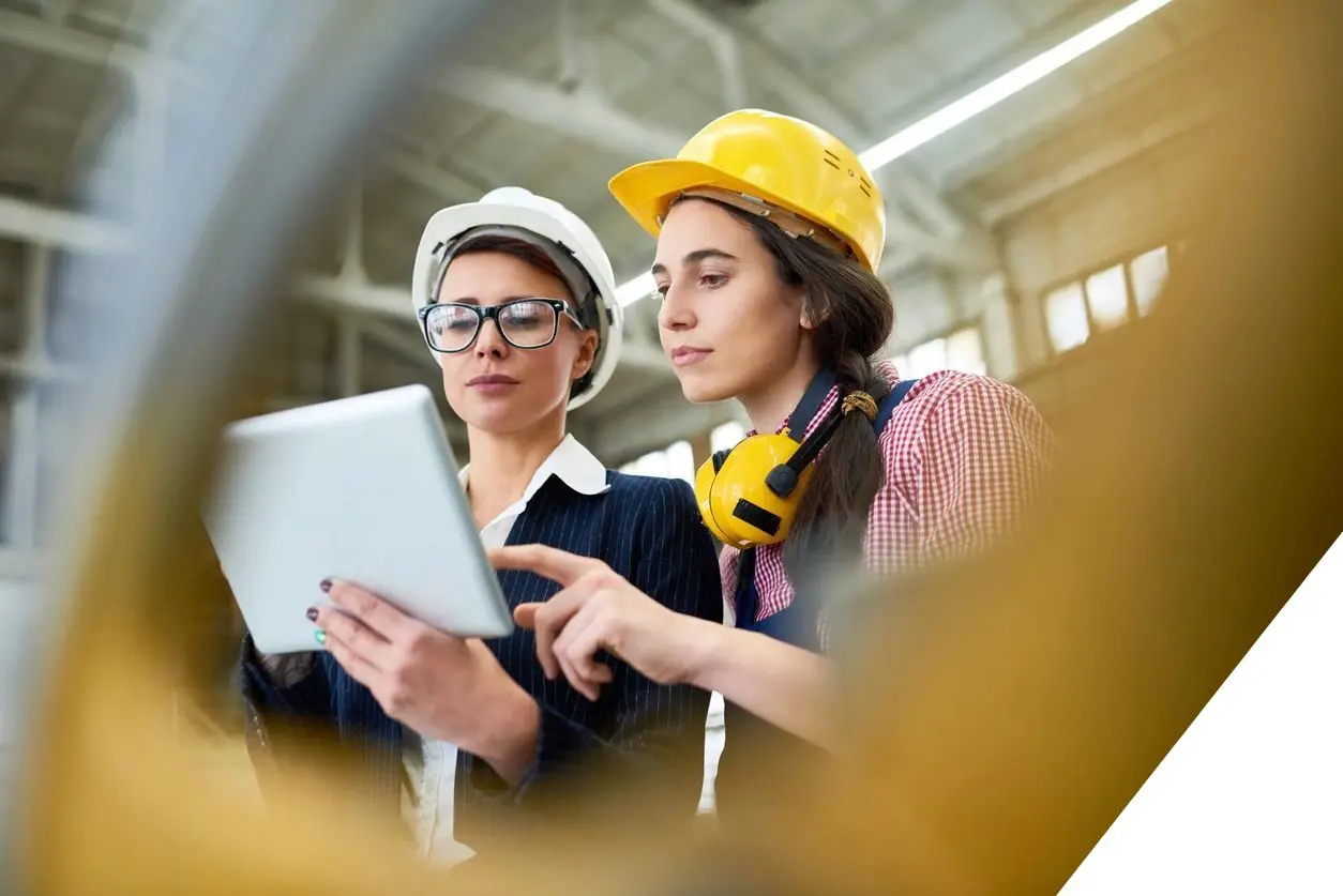 Two women in hard hats looking at a tablet.